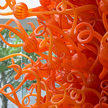 A sculpture of many curling orange tubes and bulbs, possibly glass.