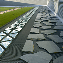 A series of linear pathways: stone, grass, glass triangles, and slate.