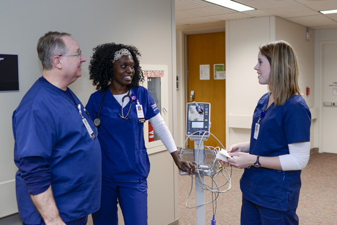 A man and two women in blue scrubs talk in a hallway