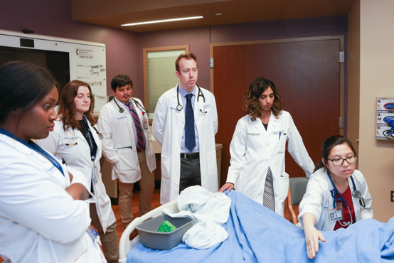 Faculty members and trainees talk with a patient at the bedside
